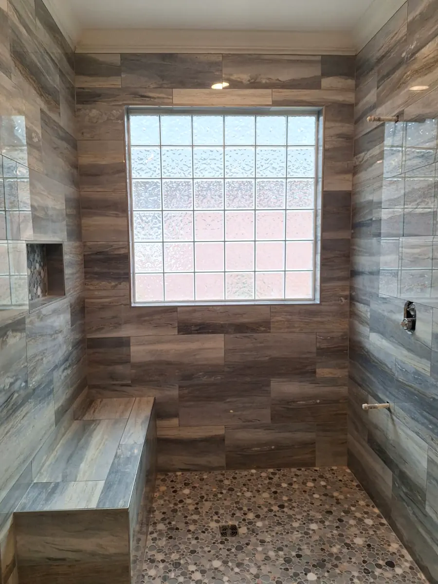 Walk-in shower with wood-look porcelain wall tile, built-in bench and pebble shower floor